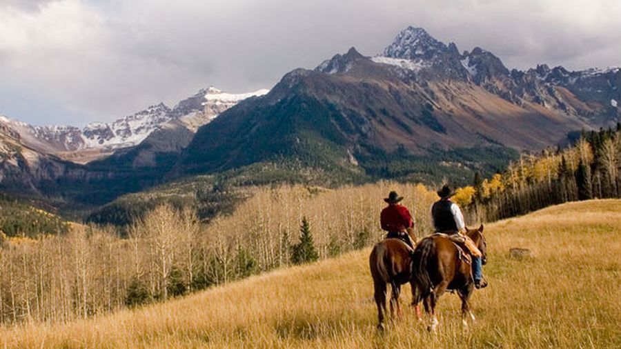 Horseback riders in a field at the base of the San Juan Mountains.